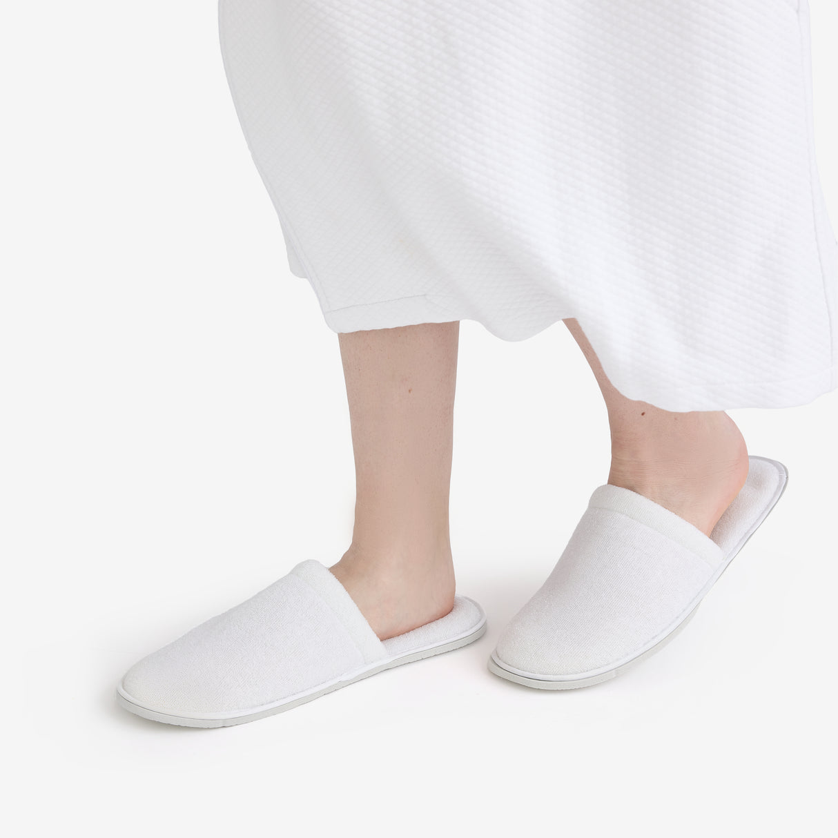 Closed toe white hotel slippers, worn by someone, on a white background.
